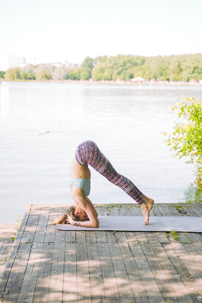 about-02 Caucasian woman doing a yoga headstand on a dock by a calm lake, showcasing balance and focus.